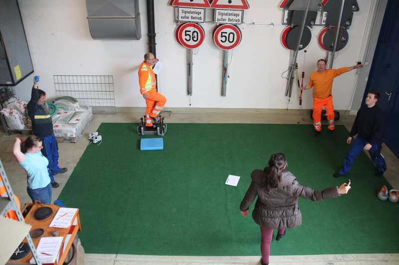 In einer Halle der Straßenmeisterei Wiesloch arbeiten Mitarbeiterinnen und Mitarbeiter des Straßenbauamtes (von links Vanessa Waxmann, Joachim Büchler, Wolfgang Weilemann, Roland Stang und Hendrik Waldi unter Anleitung der Sportwissenschaftlerin Nicolina Lerchen (vorne) an ihrer Fitness.