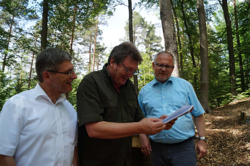 Landrat Paul Junker, Bürgermeister Eckhard Vogel und Landrat Hans-Ulrich Ihlenfeld (v.l.) lesen im Logbuch des Trekkingplatzes, in das sich alle Besucher eintragen können. (Foto: Kreisverwaltund Bad Dürkheim)