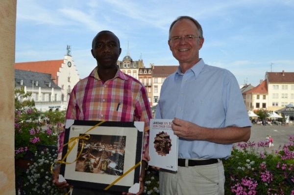 Oberbürgermeister Hans-Dieter Schlimmer übergibt dem Bürgermeister Francois Xavier Mbabazi einen Bildband über Landau und ein Bild des schneebedeckten Nikolausmarktes.