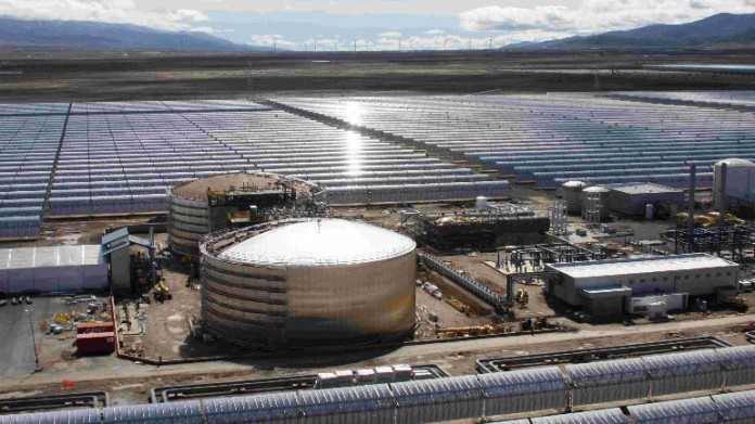 Im Hintergrund sind die Parabolrinnen des Kraftwerks zu erkennen. Beim Solarkraftwerk Andasol 1 liefern 600 Parabolrinnen-Kollektoren, die Wärmeenergie zum Betrieb des Kraftwerks. Im Vordergrund ist der Salzspeicher des Kraftwerks zu sehen.