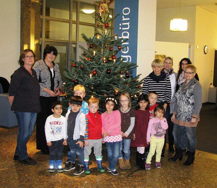 Kinder der Kindertagesstätte Mosaik der AWO mit ihrer Leiterin Lioba Ulitschnik, der Erzieherin Helga Kurz, Mitarbeiterinnen des Bürgerbüros sowie der Oberbürgermeisterin Cornelia Petzold Schick vor dem bunt geschmückten Weihnachtsbaum.