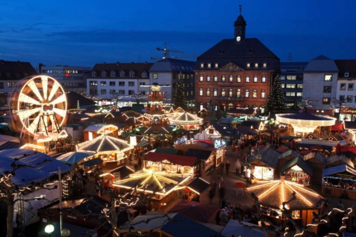 Ein Meer von Lichtern und festlich geschmückte Holzhäuschen vor der Kulisse von Hessens größtem Adventskalender: der Weihnachtsmarkt in Hanau