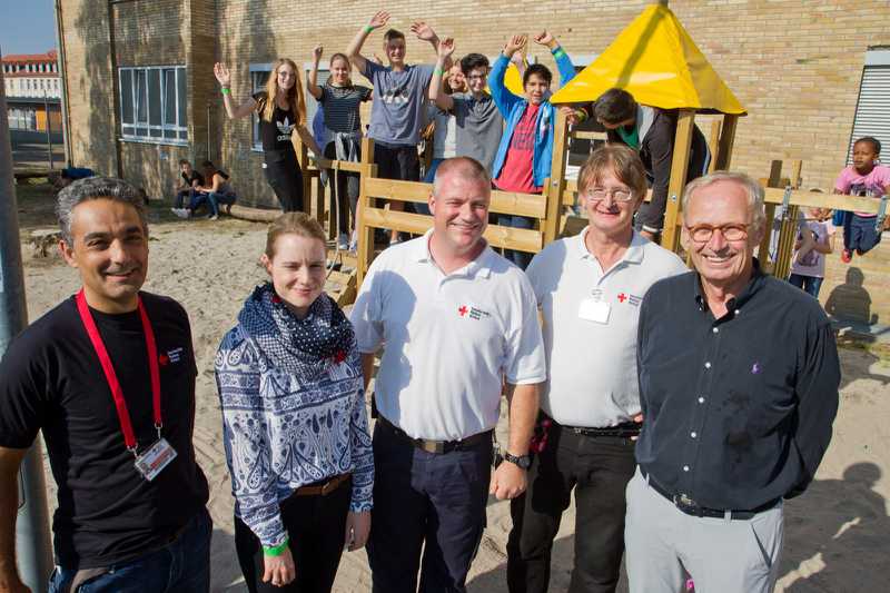 Übergabe Spielgerät, v.l.: Mitarbeiter Zekeriya Basiliyan (DRK), Klassenlehrerin Tatjana Steinke, Betriebsleiter Alexander Belloff, Ehrenamtskoordinator Hans Högel, 1. Vorsitzender Dr. Gregor Wehner (alle DRK). Im Hintergrund Schülerinnen u. Schüler der Klasse 8e sowie Kinder aus dem Michaelisdorf.