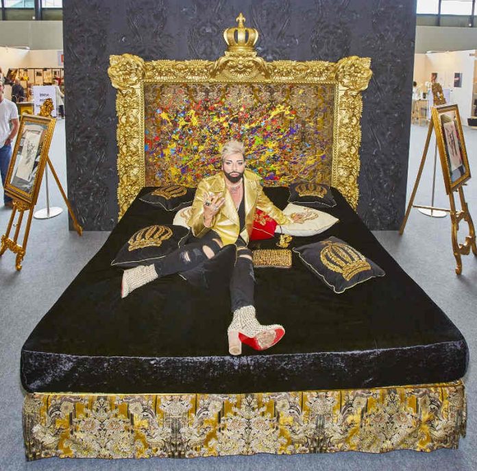 HARALD GLÖÖCKLER auf einem Boxspringbett-Unikat von Femira mit einem Kopfteil wie ein Gemälde. Das von ihm selbst gestaltete Bett feiert auf der EUNIQUE eine exklusive Preview. (Foto: KMK / Jürgen Rösner)