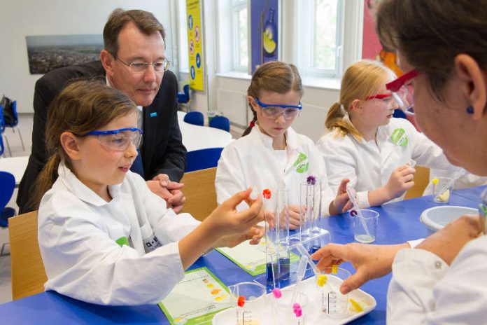 „Faszination Chemie: Michael Heinz, Vorstandsmitglied der BASF SE und Standortleiter Ludwigshafen, schaut den Jungforscherinnen im Kids‘ Lab beim Experimentieren über die Schulter.“ (Foto: BASF SE)