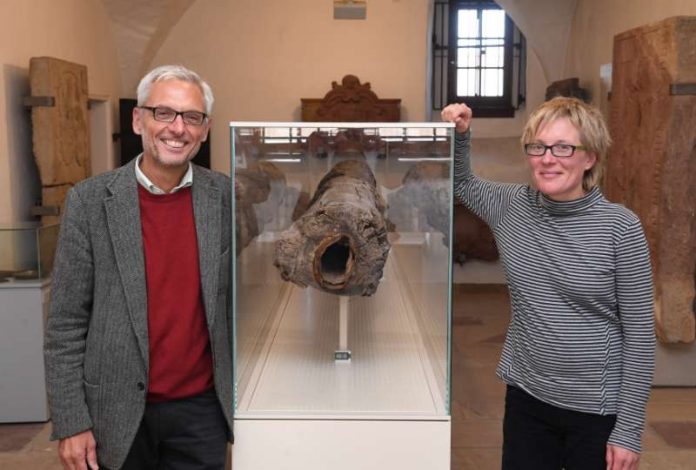 Prof. Matthias Maier und Dr. Alexandra Kaiser zeigen das historische Wasserrohr, das im Pfinzgaumuseum in einer eigens angefertigten Spezial-Vitrine gelagert wird. (Foto: Stadtwerke Karlsruhe GmbH/ ARTIS - Uli Deck)