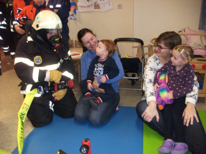 Feuerwehrmann Dennis Stark zeigt Castiel (li.) und Leonie (re.) die Bedienung eines Hohlstrahlrohres in voller Schutzausrüstung (Foto: Feuerwehr Bad Kreuznach)