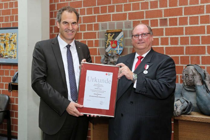 Landrat Dietmar Seefeldt überreicht Bernd Fischer (re.) die Urkunde des DRK-Landesverbands Rheinland-Pfalz zur Verleihung der Verdienstmedaille (Foto: Norman Krauß)