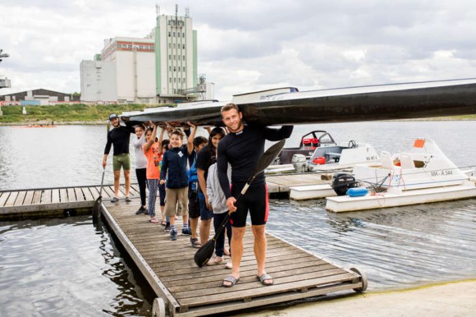 Weltmeister Max Lemke und Trainingspartner Björn Barthel (beide WSV Sandhofen) stemmen das lange Vierer-Kajak gemeinsam mit den begeisterten KinderHelden Kindern. (Foto: Team Tokio Metropolregion Rhein-Neckar)