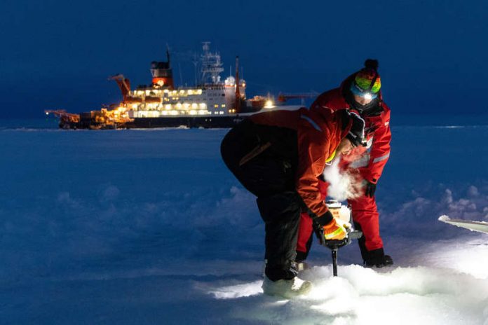 Zwei Forscher arbeiten auf dem Meereis. Im Hintergrund liegt die POLARSTERN. (Foto: Marcel Nicolaus, Alfred-Wegener-Institut)