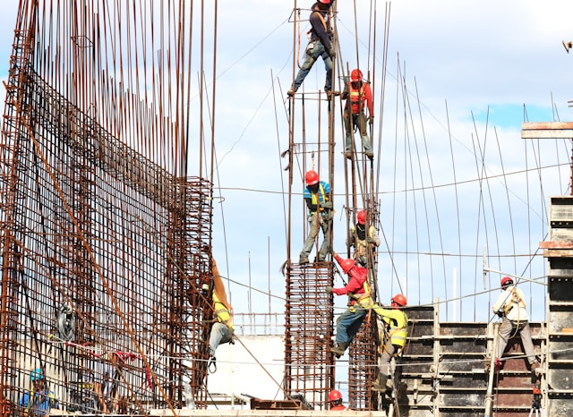 josue-isai-ramos-figueroa-qvBYnMuNJ9A-unsplash Bauarbeiter mit Schutzhelmen und Sicherheitsgurten arbeiten an einem Stahlbetongerüst auf einer Großbaustelle unter freiem Himmel
