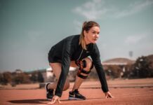 Sportlerin in Startposition auf einer Laufbahn, trägt Sportkleidung und eine Kniebandage, bereit für den Sprint.
