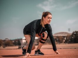 Verletzungen beim Sport: Diese Sportarten sind statistisch am gefährlichsten Sportlerin in Startposition auf einer Laufbahn, trägt Sportkleidung und eine Kniebandage, bereit für den Sprint.