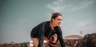 Sportlerin in Startposition auf einer Laufbahn, trägt Sportkleidung und eine Kniebandage, bereit für den Sprint.