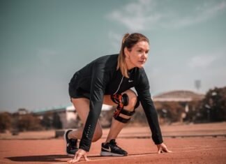Sportlerin in Startposition auf einer Laufbahn, trägt Sportkleidung und eine Kniebandage, bereit für den Sprint.
