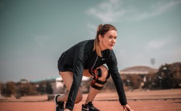 Sportlerin in Startposition auf einer Laufbahn, trägt Sportkleidung und eine Kniebandage, bereit für den Sprint.