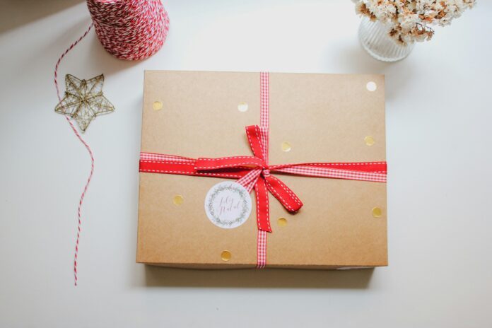jornada-produtora-daInAb9XYr8-unsplash Braune Geschenkbox mit roten und weißen Schleifen, goldenen Punkten und rundem Weihnachtssticker.
