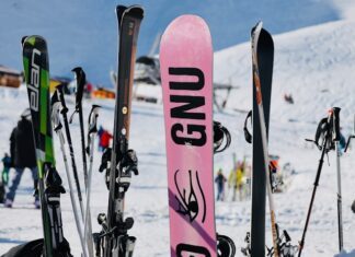 Verschiedene Skier und ein Snowboard stehen aufrecht im Schnee vor einer verschneiten Bergkulisse – Symbol für moderne und flexible Skiausrüstung, wie sie Wintersportler:innen bei Alpy.com in Nauders mieten können