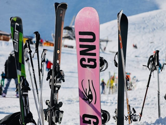 valerii-ladomyriak--1ltNh_S6i0-unsplash Verschiedene Skier und ein Snowboard stehen aufrecht im Schnee vor einer verschneiten Bergkulisse – Symbol für moderne und flexible Skiausrüstung, wie sie Wintersportler:innen bei Alpy.com in Nauders mieten können